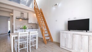 Uma cozinha moderna com escada de madeira, área de jantar com mobiliário branco e uma TV em um armário de madeira.
