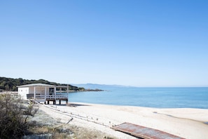 Una playa con un edificio blanco, una terraza de madera y un cielo azul despejado.