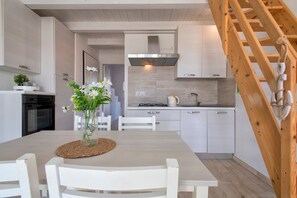 A modern kitchen with white cabinets, a stainless steel range hood, and a wooden staircase.