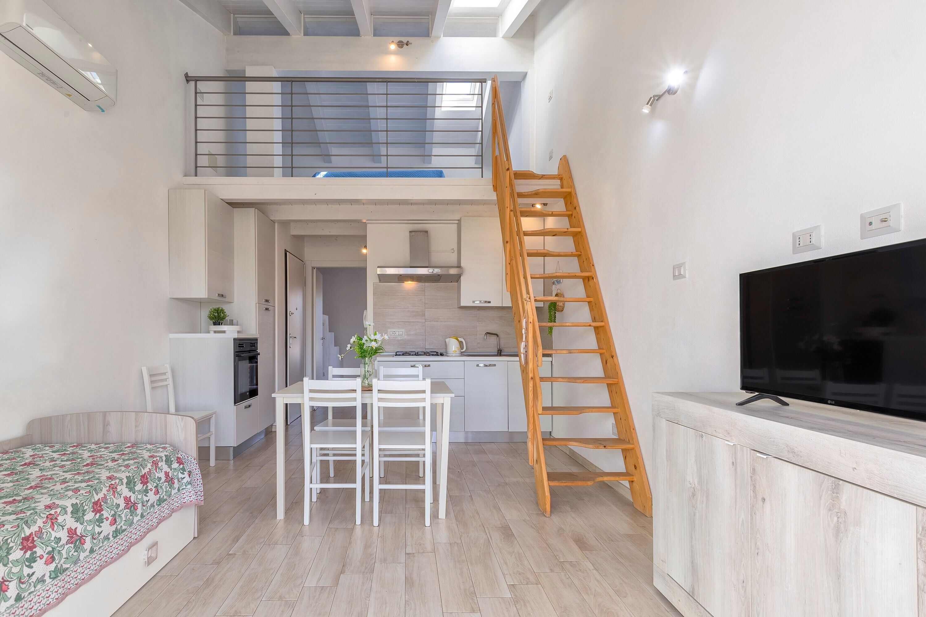 Un espace de vie compact comprenant une chambre en mezzanine, un coin repas, une cuisine et un téléviseur.