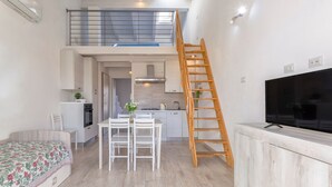 Um espaço compacto com um quarto no mezanino, área de jantar, cozinha e televisão.