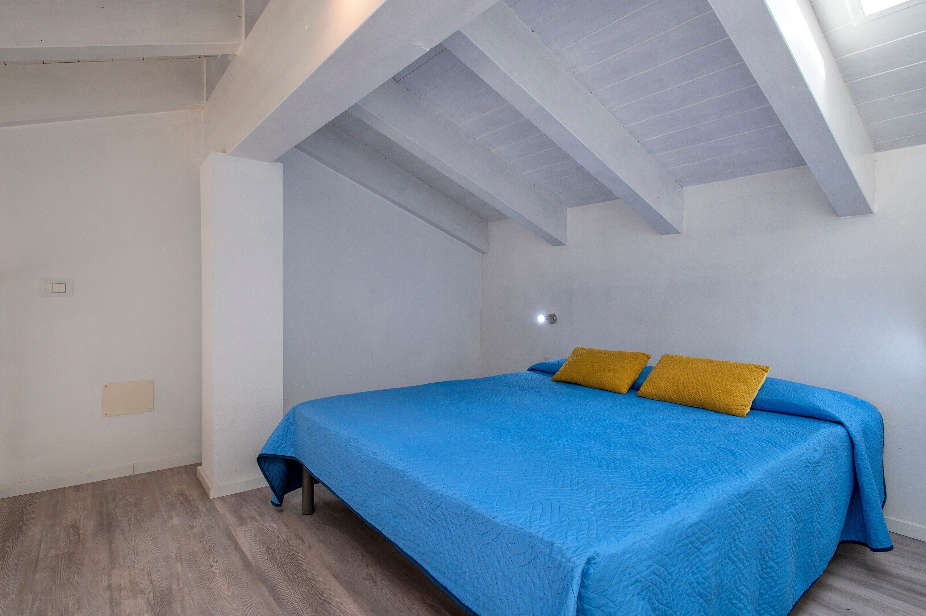 A bedroom with a sloped ceiling, a bed with blue bedding, and a wooden floor.