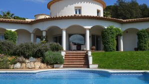 En villa i medelhavsstil med en swimmingpool, en täckt uteplats och en välskött trädgård.