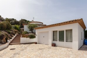 A building with a tiled roof, a garage door, and a stone-paved entrance. - Villa Blanca-------- (Calonge)