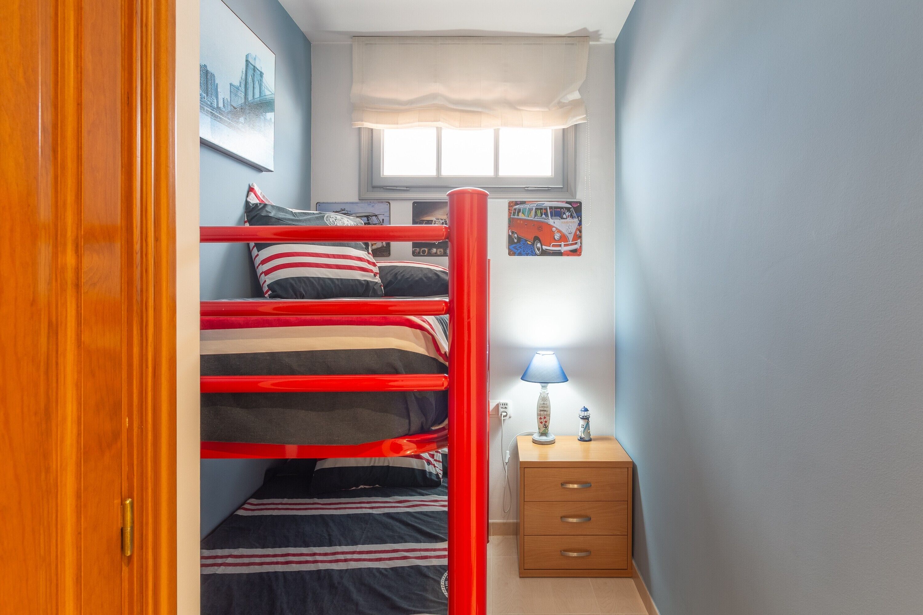 Una cama litera con ropa de cama a rayas, una lámpara de noche y una mesita de noche de madera.