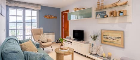A living room with a sofa, armchair, TV, and decorative items.