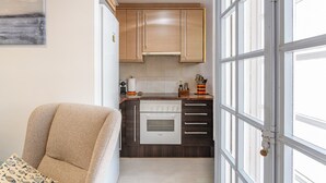 A compact kitchen with wooden cabinets, a white oven, and a window. - Sunset Apartment on the Paseo de Mar in Front of the Beach with Wi-Fi (Sant Antoni de Calonge)