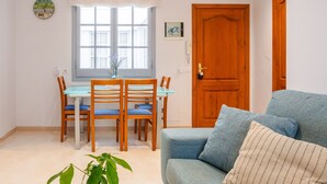 A room with a dining table, chairs, a blue sofa, a wooden door, and a window with a view. - Sunset Apartment on the Paseo de Mar in Front of the Beach with Wi-Fi (Sant Antoni de Calonge)