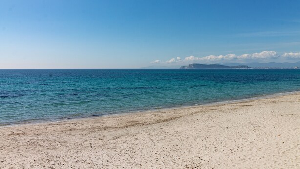 A beach with clear water, a sandy shore, and distant mountains.