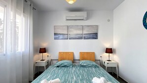 Ein Hotelzimmer mit einem Bett, zwei Nachttischen, einer wandmontierten Klimaanlage und einem Fenster mit Vorhängen.