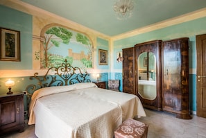 Un dormitorio con cama, armario, mesita de noche, lámpara y un mural en la pared.