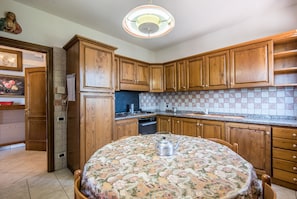 A kitchen with wooden cabinets, a tiled backsplash, a round table with a floral tablecloth, and a hanging light fixture. - Villa in the Heart of Chianti — Peace, Views, and Authentic Tuscany (Certaldo - Firenze)