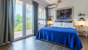 Un dormitorio con una cama grande, un balcón con cortinas, un cuadro en la pared y una estantería con una lámpara.