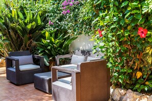 Een terras met rieten meubilair, omgeven door weelderig groen en bloeiende planten.