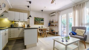 Una cocina moderna con armarios blancos, una zona de comedor con mesa de madera y un sillón gris.