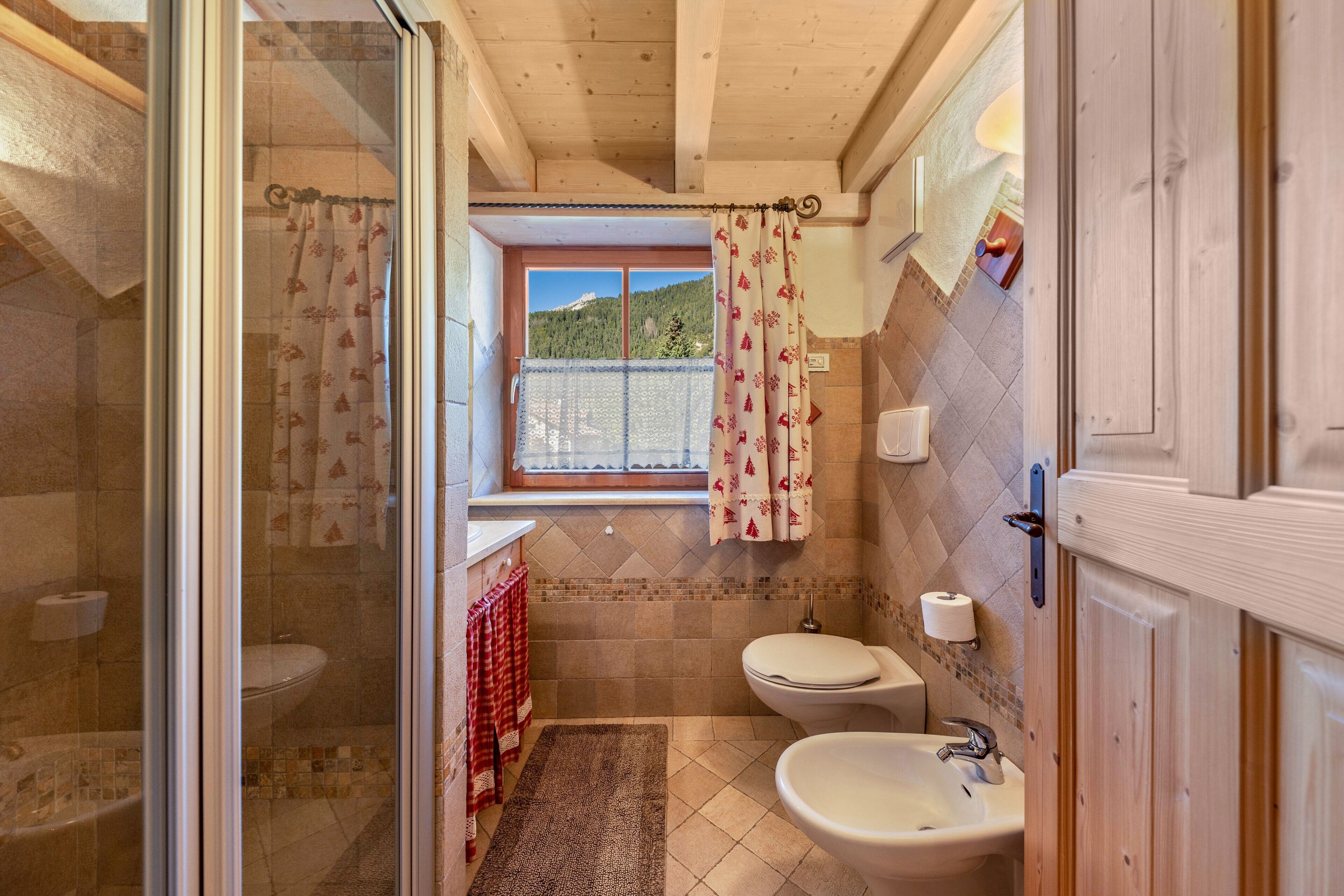 A bathroom with a shower, toilet, sink, and a window with a view of a mountain.