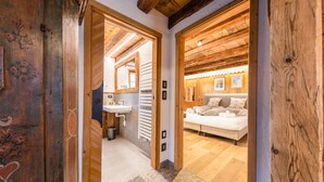 Un couloir intérieur en bois mène à une chambre à coucher équipée d’un lit, d’une table de chevet et d’une petite table de nuit.