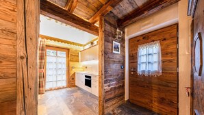Un intérieur en bois comprenant un coin cuisine, une porte ornée d’un rideau en dentelle et une fenêtre à carreaux.