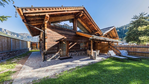 Une cabane en bois avec un toit en pente, un chemin de pierres menant à l’entrée et une cour verdoyante avec des chaises longues.