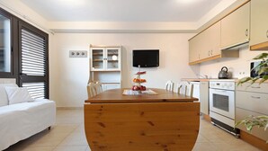 Eine kompakte Küche mit Esstisch aus Holz, einem eingebauten Backofen und einem an der Wand montierten Fernseher.