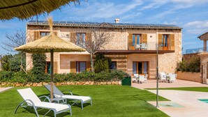 Ein zweistöckiges Steinhaus mit Balkon, Pool und gepflegtem Rasen mit Liegestühlen.