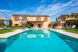 A pool with lounge chairs, a stone building with balconies, and a clear blue sky. - Apartment S Hort Can Capità Familiar Superior 2 close to the Sea with Shared Pool & Wi-Fi (Ariany)