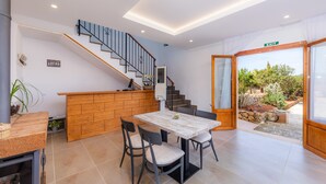 A modern interior with a wooden dining table, chairs, a staircase, and a view through a glass door.