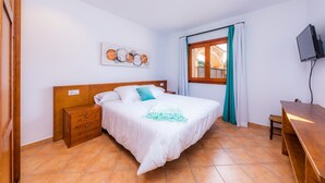 A bedroom with a bed, a wooden nightstand, a desk, a television, and a window with curtains.