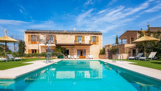 A pool with lounge chairs, a stone building with balconies, and a clear blue sky.
