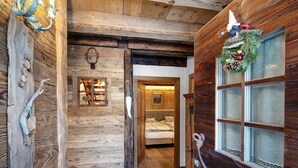 L’intérieur d’une cabane en rondins, avec un lit, des murs en bois, une guirlande décorative et une fenêtre avec un rideau.