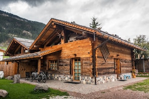 A rustic wooden cabin with a stone foundation, a porch with a bench, and a bicycle parked outside.