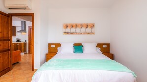 A bedroom with a bed, a nightstand, a wall-mounted artwork, and a view into the adjacent kitchen.