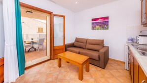 A compact living space with a sofa, a small table, a kitchen area, and a sliding glass door leading to an outdoor patio.