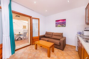 Un espacio habitable compacto con sofá, una mesita, zona de cocina y puerta corrediza de vidrio que da a un patio exterior.