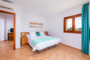 Une chambre à coucher comprenant un lit, une table de chevet, un téléviseur, une fenêtre avec des rideaux et une œuvre d’art accrochée au mur.