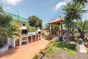 Et udendørs køkkenområde med grill, en træpergola og en stentumskulptur.