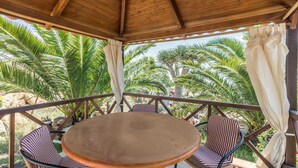 A covered outdoor seating area with a round table and striped chairs, surrounded by palm trees. - Pet-Friendly Apartment B Armonia Rural with Sea View, Terrace, Shared Pool & Wi-Fi (Granadilla de Abona)
