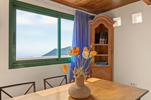 A dining area with a table, chairs, a vase with flowers, a bookshelf, and a window with a view. - Pet-Friendly Apartment B Armonia Rural with Sea View, Terrace, Shared Pool & Wi-Fi (Granadilla de Abona)
