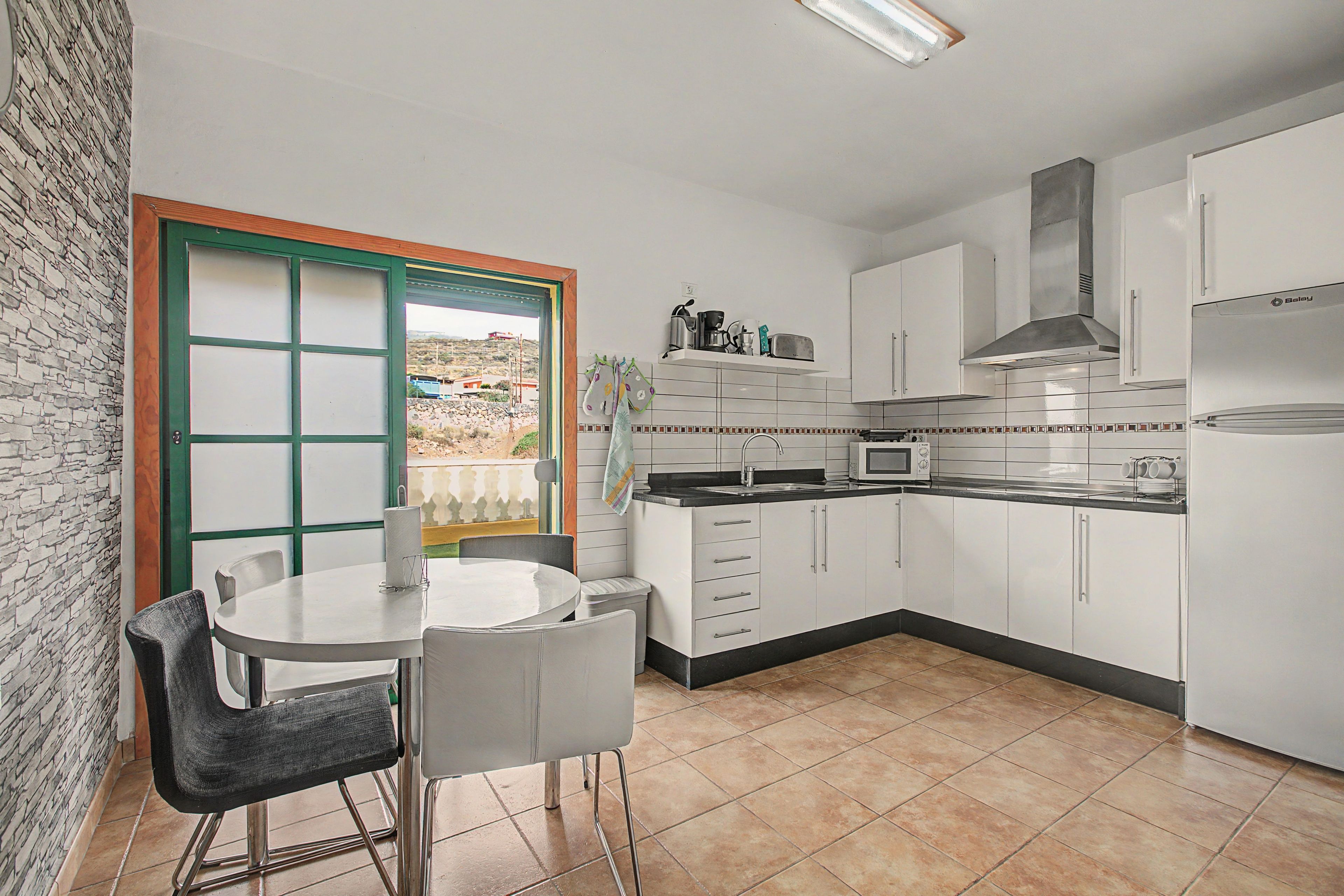 A compact kitchen with white cabinets, a dining table with chairs, and a view through a window.