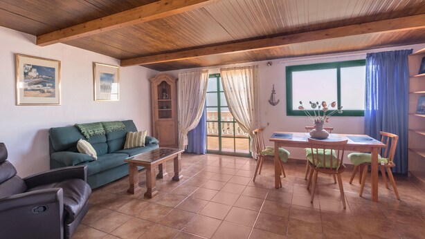 A living room with a sofa, a dining table with chairs, a wooden ceiling, and a window with curtains. - Pet-Friendly Apartment B Armonia Rural with Sea View, Terrace, Shared Pool & Wi-Fi (Granadilla de Abona)