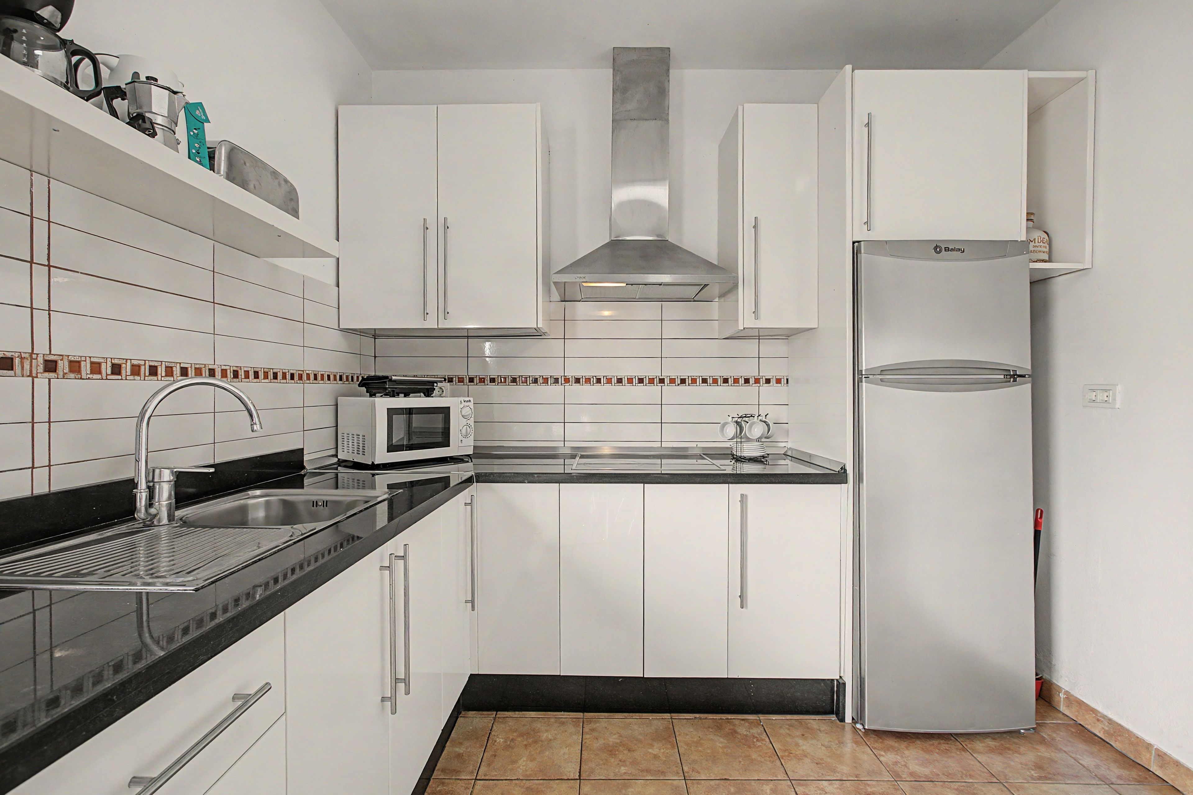 A kitchen with white cabinets, a stainless steel refrigerator, a microwave, and a sink with a modern faucet.