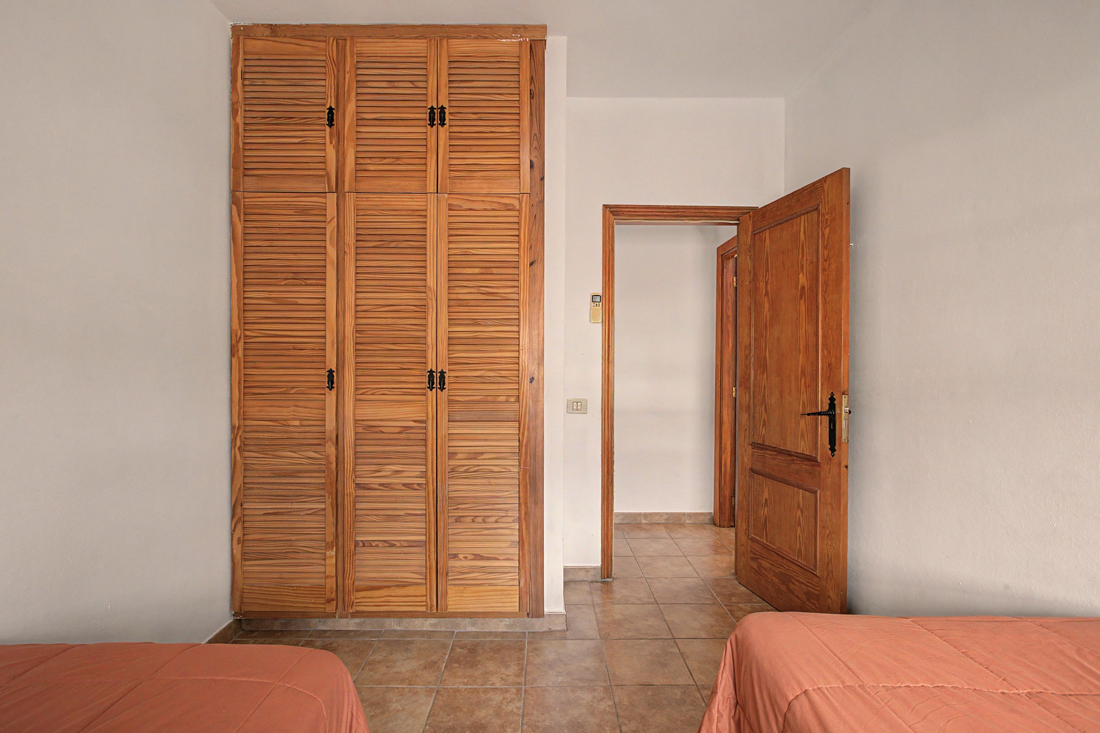 A bedroom with a wooden wardrobe, a single bed, and a door leading to another room.