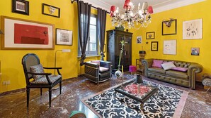 Una sala de estar con pared amarilla, una araña, un sofá, un sillón y una mesa de centro.