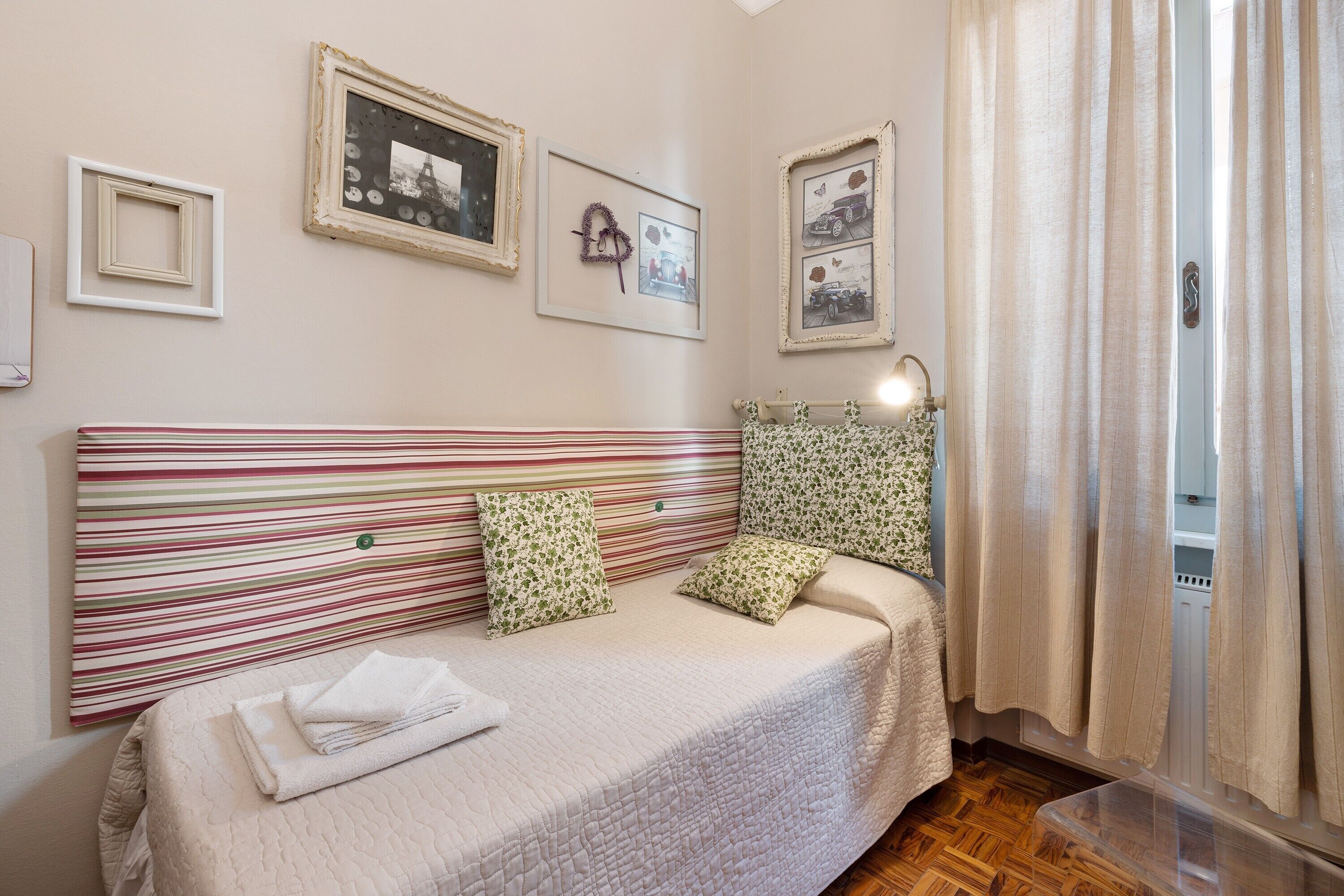 A neatly made bed with a striped headboard, a bedside lamp, and a window with curtains.