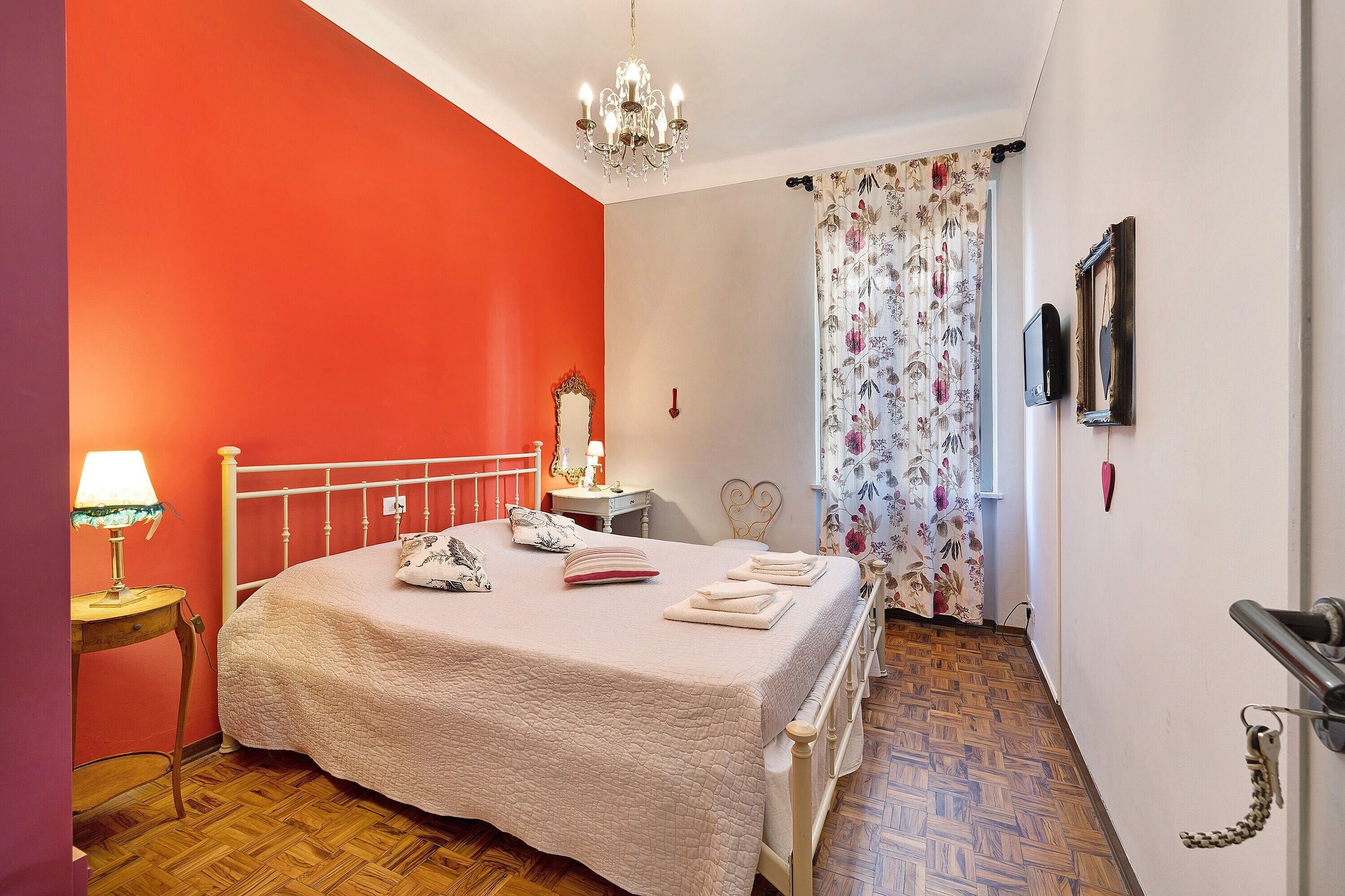 Un dormitorio con cama, mesita de noche, lámpara, espejo, candelabro y puerta con llavero.