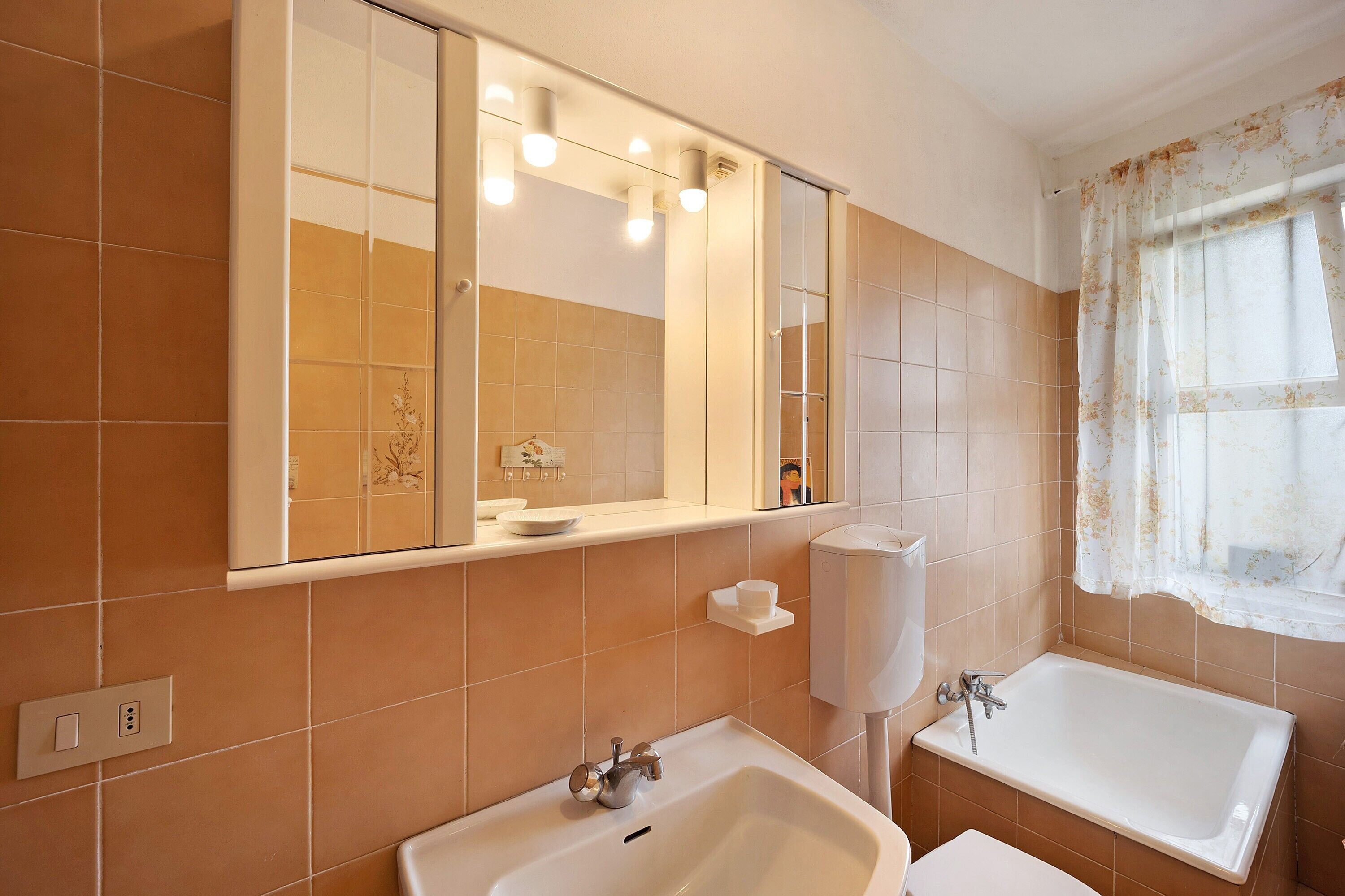 A bathroom with a large mirror, a sink, a bathtub, and a toilet.