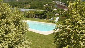 Una piscina rodeada de vegetación, césped y una colina al fondo.
