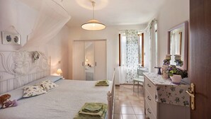 Un dormitorio con cama, mesita de noche, cómoda, espejo y una puerta que da a otra habitación.