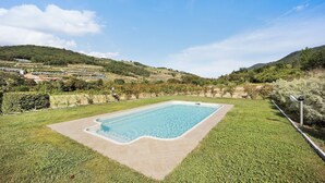 A rectangular swimming pool with a tiled edge, surrounded by a well-maintained lawn, set against a backdrop of rolling hills and a clear sky.
