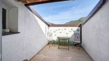 A small patio with a table and two chairs, a window, and a view of a green hill.
